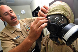 A U.S. Navy chemical/biological defense officer helps a sailor don a joint-service lightweight integrated suit technology chemical-protective ensemble during a chemical, biological, radiological and nuclear defense training course. (U.S. Navy photo)